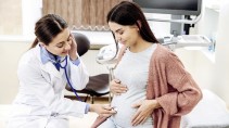 Eine Gynäkologin hört den Bauch einer schwangeren Frau mit einem Stetoskop ab.